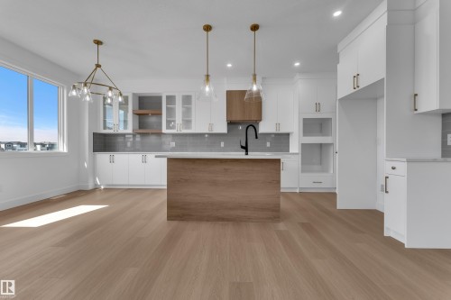 Open-concept kitchen with a wood-finish island, white cabinetry, integrated appliances, and wood-finish flooring - 4212 63 Street, Beaumont, AB 