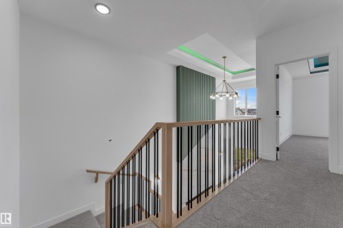 Open landing with light-colored carpeting, a contemporary chandelier, a coffered ceiling with accent lighting, and a slatted accent wall - 4212 63 Street, Beaumont, AB 