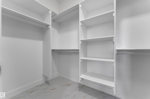 Built-in closet system with multiple shelving units and hanging rods, complemented by white walls and tile flooring - 4212 63 Street, Beaumont, AB 