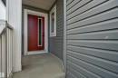 Red entry door with vertical glass insert, grey horizontal siding, and concrete porch - 4212 63 Street, Beaumont, AB 