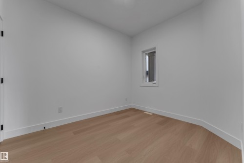 Light wood-finish flooring with white baseboards, a white door with matte black hardware, and a single window with white trim - 4212 63 Street, Beaumont, AB 