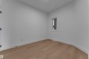 Light wood-finish flooring with white baseboards, a white door with matte black hardware, and a single window with white trim - 4212 63 Street, Beaumont, AB 