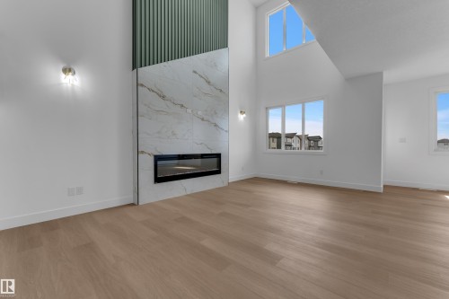 Vaulted ceiling, two-story accent wall with decorative paneling and large format tile, built-in linear fireplace, and wood-finish flooring - 4212 63 Street, Beaumont, AB 