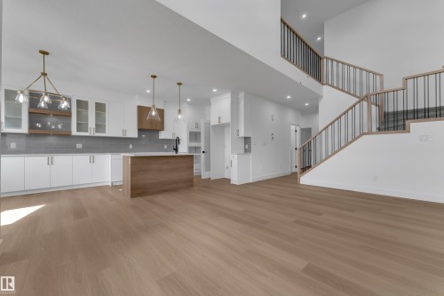 Wood-finish flooring throughout, kitchen with white cabinetry and an island, grey subway tile backsplash, and a multi-level staircase with black metal balusters - 4212 63 Street, Beaumont, AB 