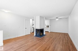 Open-concept living area featuring wood-finish flooring, a white brick fireplace, and a ceiling fan - 