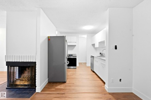 Wood-finish flooring throughout, bright white walls, fireplace with tile surround, stainless steel appliances, and white cabinetry - 258 Surrey Gardens Nw, Edmonton, AB 