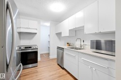 Kitchen with wood-finish flooring, white cabinetry, light-toned countertops, and stainless steel appliances - 