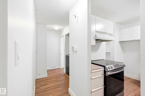 Wood-finish flooring throughout, bright white walls, contemporary white cabinetry, stainless steel range with overhead hood fan, and integrated shelving - 258 Surrey Gardens Nw, Edmonton, AB 