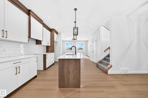 Modern kitchen featuring white cabinetry, subway tile backsplash, a center island with sink, and wood-finish flooring - 9 Tilia Place, Spruce Grove, AB 