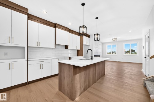 Open-concept kitchen featuring an island with a built-in sink, white cabinetry with wood-finish accents, and a tile backsplash - 9 Tilia Place, Spruce Grove, AB 