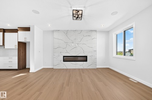 Wood-finish flooring throughout, a modern linear fireplace with a large-format tile surround, recessed lighting, and a contemporary ceiling fixture - 9 Tilia Place, Spruce Grove, AB 