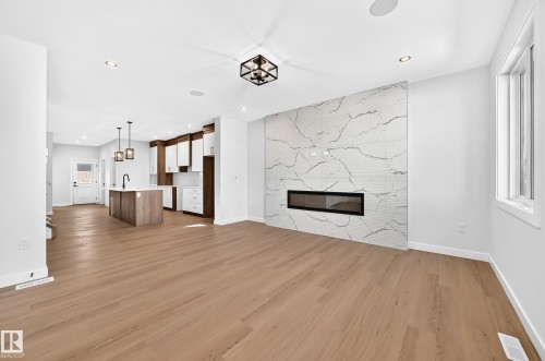 Expansive open-concept space featuring wood-finish flooring, a contemporary fireplace with a stone-look tile surround, recessed lighting, and a kitchen with an island and pendant lighting - 9 Tilia Place, Spruce Grove, AB 
