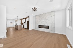 Expansive open-concept space featuring wood-finish flooring, a contemporary fireplace with a stone-look tile surround, recessed lighting, and a kitchen with an island and pendant lighting - 