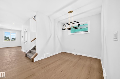 Wood-finish flooring, staircase with carpeted treads and wood handrails, recessed ceiling lighting, and a modern rectangular chandelier - 9 Tilia Place, Spruce Grove, AB 