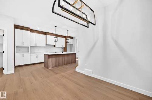 Light wood-finish flooring throughout, kitchen featuring white shaker cabinetry, wood-finish island, white subway tile backsplash, and a modern rectangular chandelier - 9 Tilia Place, Spruce Grove, AB 