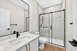 Modern bathroom with a white vanity, integrated sink, matte black fixtures, wood-finish flooring, and a glass-enclosed shower with subway tile surround - 