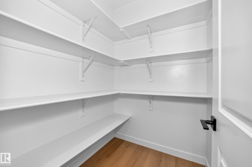 Corner pantry with multiple white built-in shelves, wood-finish flooring, and a door with matte black hardware - 9 Tilia Place, Spruce Grove, AB 
