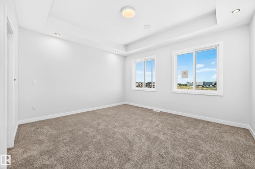 Tray ceiling with recessed lighting, central flush mount fixture, two large windows, and neutral carpeting - 9 Tilia Place, Spruce Grove, AB 