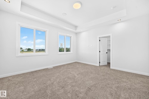 Tray ceiling featuring recessed lighting and a central flush-mount fixture, two multi-pane windows, and a walk-in closet with built-in shelving - 9 Tilia Place, Spruce Grove, AB 