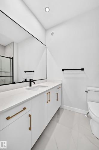 White vanity with gold-finish hardware, a large frameless mirror, and a sleek black-finish faucet - 9 Tilia Place, Spruce Grove, AB 
