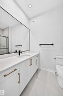 White vanity with gold-finish hardware, a large frameless mirror, and a sleek black-finish faucet - 