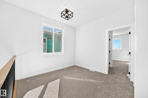 White walls, neutral carpet, black framed semi-flush mount light fixture, white window frame, and a white interior door with black hardware - 9 Tilia Place, Spruce Grove, AB 