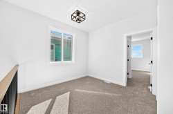 White walls, neutral carpet, black framed semi-flush mount light fixture, white window frame, and a white interior door with black hardware - 
