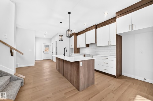 Kitchen featuring wood-finish flooring, a central island with a solid surface countertop, white subway tile backsplash, and two-tone cabinetry with white upper and wood-finish lower cabinets - 9 Tilia Place, Spruce Grove, AB 