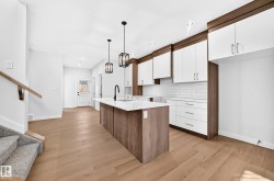 Kitchen featuring wood-finish flooring, a central island with a solid surface countertop, white subway tile backsplash, and two-tone cabinetry with white upper and wood-finish lower cabinets - 