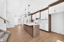 Kitchen featuring wood-finish flooring, a central island with a solid surface countertop, white subway tile backsplash, and two-tone cabinetry with white upper and wood-finish lower cabinets - 9 Tilia Place, Spruce Grove, AB 
