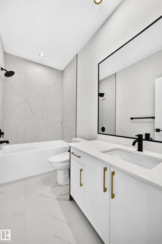 White vanity with gold-finish hardware and integrated sink, black-framed mirror, and a white bathtub with black fixtures - 9 Tilia Place, Spruce Grove, AB 