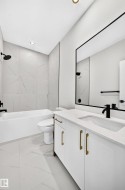 White vanity with gold-finish hardware and integrated sink, black-framed mirror, and a white bathtub with black fixtures - 