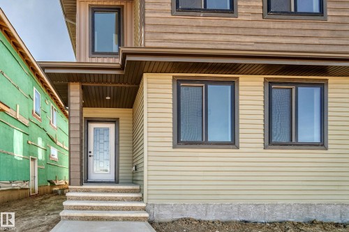 Multi-toned horizontal siding exterior with dark-framed windows, a white entry door with decorative glass, and a covered entry with stone-finish steps - 9 Tilia Place, Spruce Grove, AB 