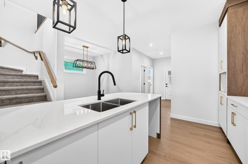 Kitchen island with a double basin sink and matte black faucet, accented by white cabinetry with gold-tone hardware - 9 Tilia Place, Spruce Grove, AB 