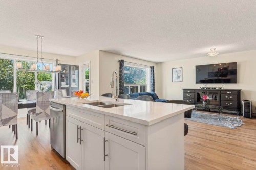 Open-concept living area featuring a kitchen island with a double basin sink, white cabinetry, and light-toned countertops - 1007 Macewan Close Sw, Edmonton, AB - Indoor