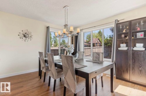 Dining space featuring wood-finish flooring, a contemporary chandelier, large windows with exterior views, and built-in display cabinetry - 1007 Macewan Close Sw, Edmonton, AB - Indoor Photo Showing Dining Room