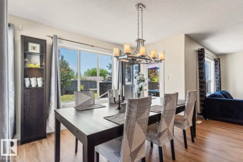 Dining area with wood-finish flooring, a contemporary chandelier, and a built-in dark wood shelving unit - 1007 Macewan Close Sw, Edmonton, AB - Indoor Photo Showing Dining Room