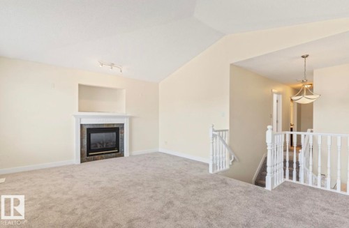 Open-concept room featuring a fireplace with a white mantel and stone surround, built-in recessed niche, vaulted ceiling, and new gray carpet - 1007 Macewan Close Sw, Edmonton, AB - Indoor Photo Showing Living Room With Fireplace