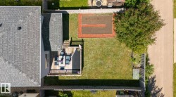 Expansive fenced backyard featuring a wood deck, manicured lawn, established tree, and a garden bed with defined borders - 