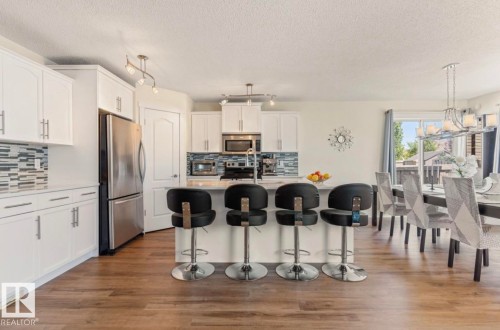 Kitchen featuring an island with seating, white cabinetry, stainless steel appliances, and wood-finish flooring - 1007 Macewan Close Sw, Edmonton, AB - Indoor Photo Showing Kitchen With Stainless Steel Kitchen With Upgraded Kitchen