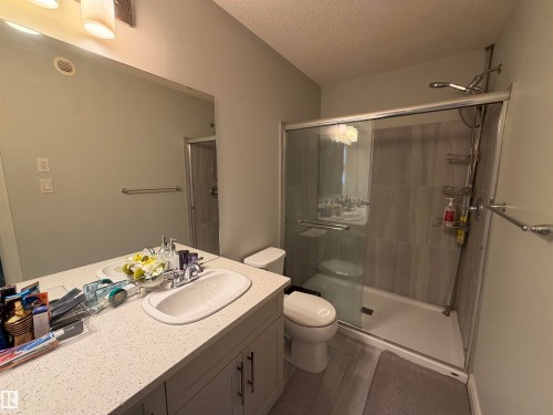 Walk-in shower with clear glass enclosure, gray subway tile, and a single vanity with an integrated sink and light-toned countertop - 2628 Donaghey Crescent Sw, Edmonton, AB 