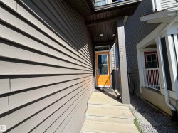 Concrete front steps leading to an orange entry door with glass panels, complemented by gray siding and a dark brown overhead soffit - 