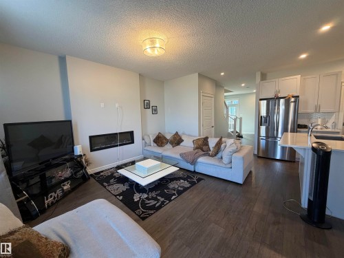 Open-concept living area with wood-finish flooring, a linear electric fireplace, and a contemporary ceiling light fixture - 2628 Donaghey Crescent Sw, Edmonton, AB 