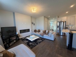 Open-concept living area with wood-finish flooring, a linear electric fireplace, and a contemporary ceiling light fixture - 