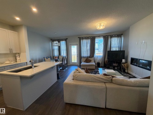 Open-concept living space with wood-finish flooring, a kitchen island with an undermount sink, recessed lighting, and a built-in fireplace feature - 2628 Donaghey Crescent Sw, Edmonton, AB 