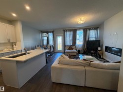 Open-concept living space with wood-finish flooring, a kitchen island with an undermount sink, recessed lighting, and a built-in fireplace feature - 