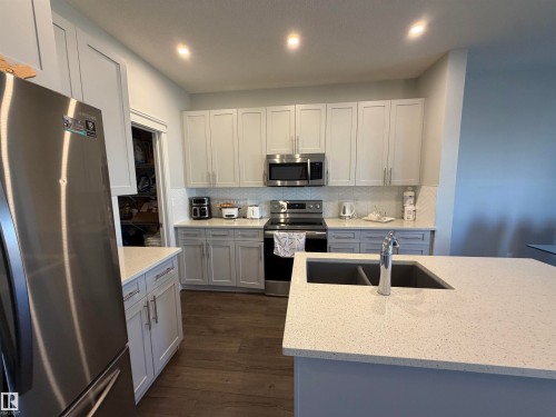 Kitchen featuring stainless steel appliances, light-toned cabinetry, a spacious island with an undermount sink, recessed lighting, and wood-finish flooring - 2628 Donaghey Crescent Sw, Edmonton, AB 