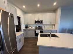 Kitchen featuring stainless steel appliances, light-toned cabinetry, a spacious island with an undermount sink, recessed lighting, and wood-finish flooring - 