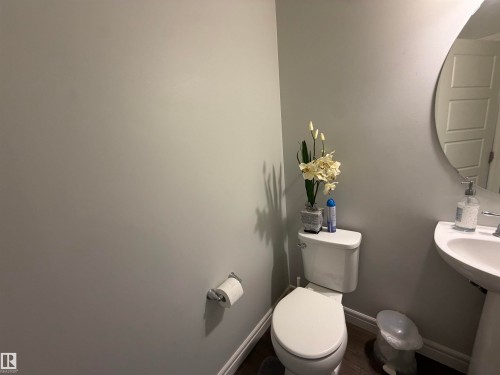 White pedestal sink, modern round mirror, and toilet with chrome fixtures - 2628 Donaghey Crescent Sw, Edmonton, AB 