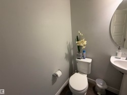 White pedestal sink, modern round mirror, and toilet with chrome fixtures - 